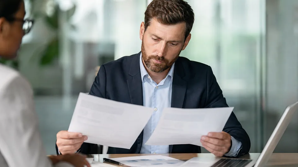 Manager comparing two vendor contracts on a meeting table with a calculator