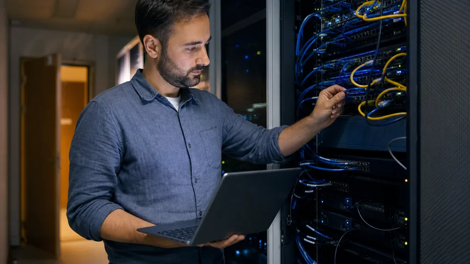 Engineer holding a laptop while checking cables in a server rack